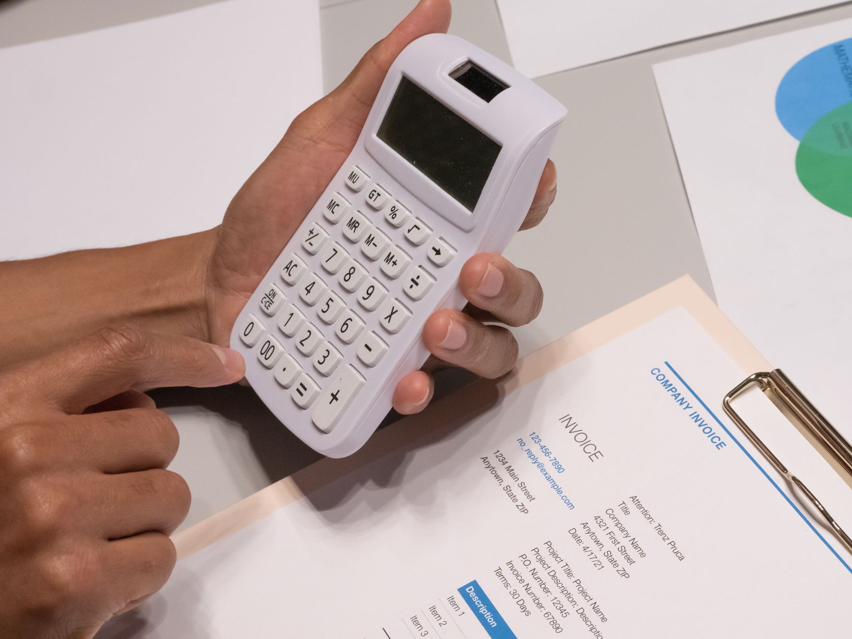 A hand working through an invoice with a calculator.