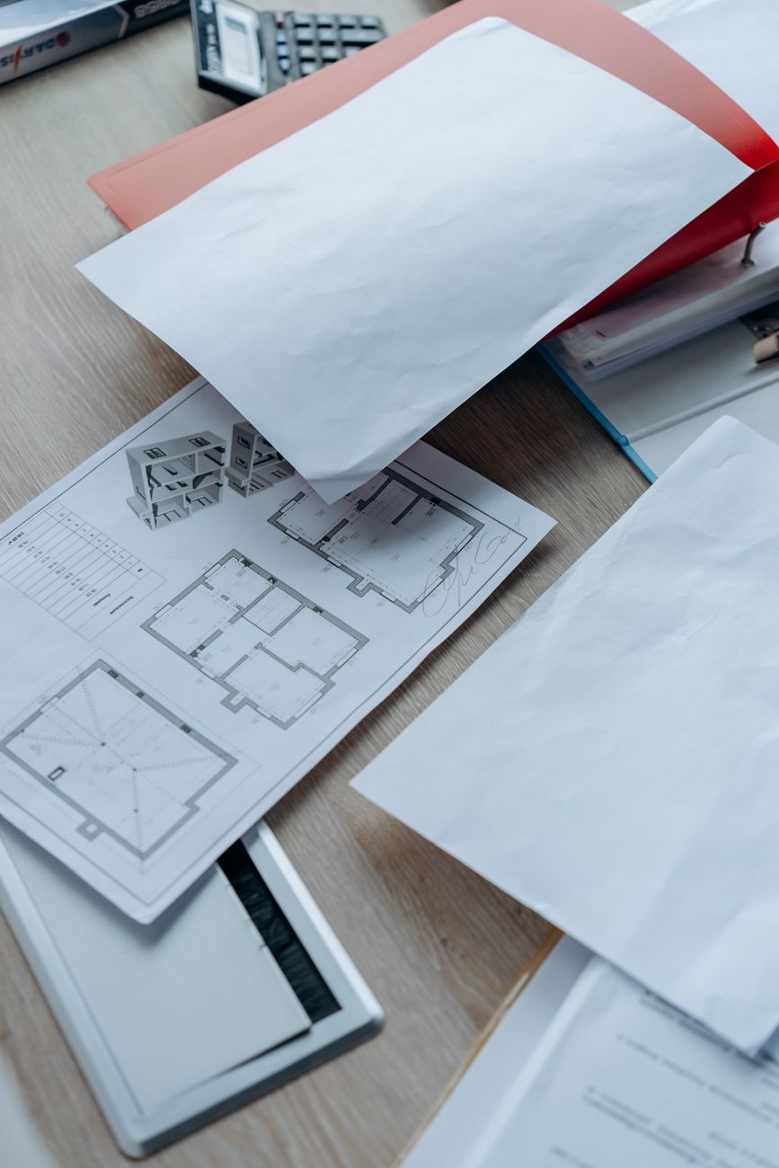 Drawings and inspection paperwork gathered on a desk, the raw material of a handover pack.